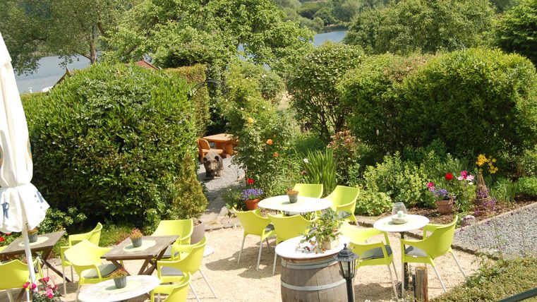 Ein einladender Garten mit grünen Büschen und bunten Blumen. Es sind Tische und Stühle im Freien aufgebaut, ideal für eine entspannte Auszeit.