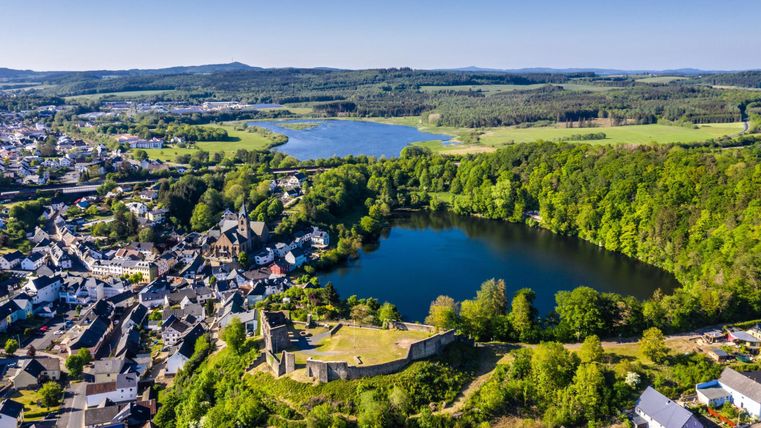 A picturesque landscape with a lake and lush greenery. In the background, there is a small town and gentle hills.