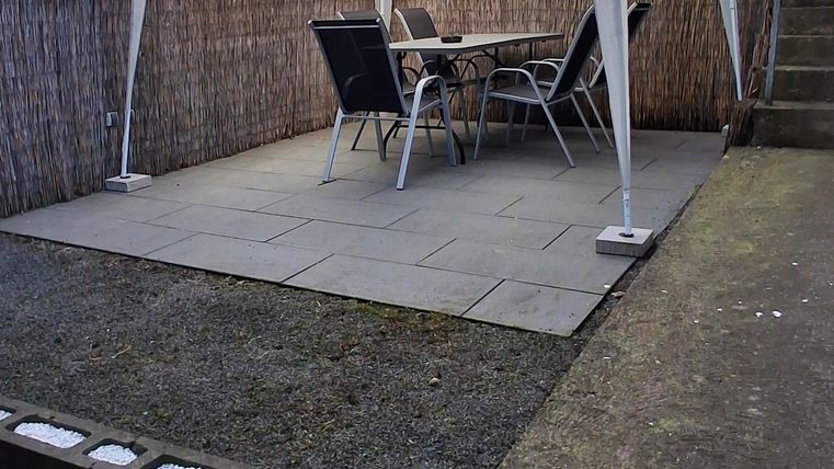 Ein gemütlicher Gartenbereich mit einem weißen Pavillon und einem Tisch mit Stühlen. Der Boden ist mit Platten ausgelegt und es gibt eine Wand aus Holzelementen.
