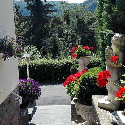 Ein schöner Garten mit bunten Blumen und Skulpturen. Der Blick reicht auf eine grüne Landschaft im Hintergrund.
