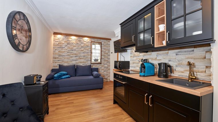 A modern kitchenette with wooden surfaces and elegant black cabinets. In the background, there is a cozy seating area with a blue sofa and a beautiful wall.
