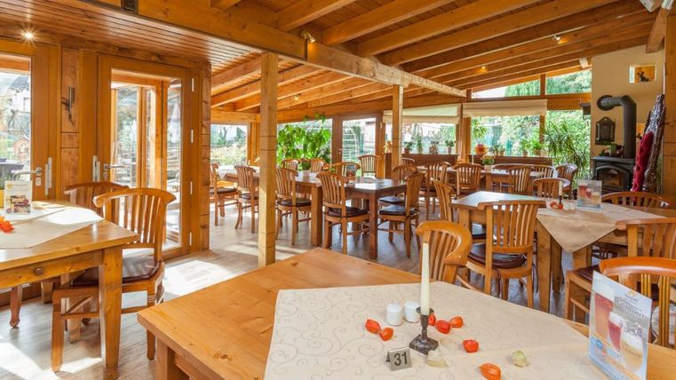 Cozy conservatory with wooden furniture, large windows, and plants. The tables are adorned with tablecloths and decorations.