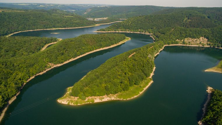 Eine malerische Landschaft mit einem gewundenen Fluss und bewaldeten Ufern. Die grüne Umgebung und das klare Wasser laden zur Erholung ein.