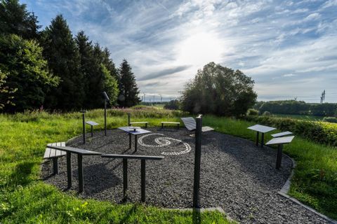 A round area with tables and display boards in a green landscape. In the background, trees and a clear sky are visible.
