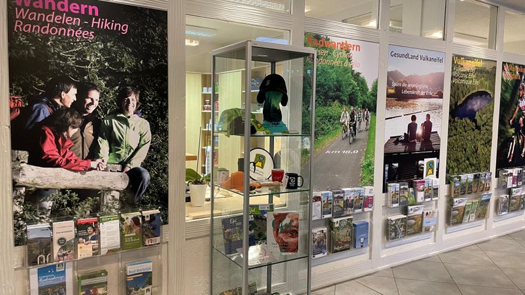 Ein Informationsbereich mit Plakaten zum Wandern und Freizeitaktivitäten. In einer Vitrine sind verschiedene Produkte und Broschüren ausgestellt.