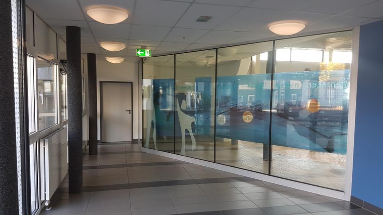 A bright hallway with large glass windows. Blue elements and modern lighting can be seen on the wall.