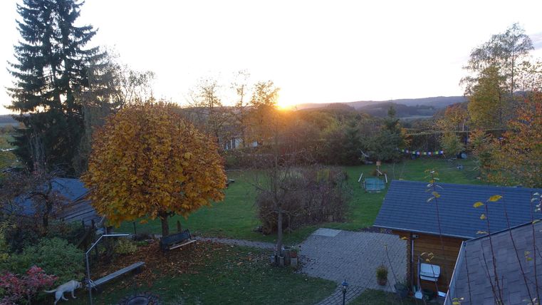A beautiful autumn garden with colorful foliage and gentle hills in the background. The sun is slowly setting on the horizon.