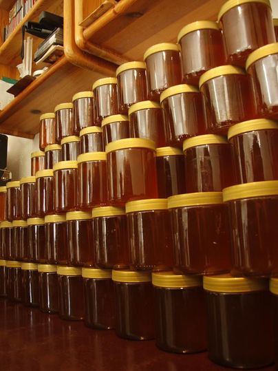 Gestapelte Honiggläser mit gelben Deckeln auf Holzregalen in einem Lagerraum.