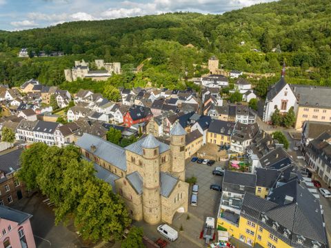 Een historische stadszicht met een markante kerk op de voorgrond. Op de achtergrond zijn groene heuvels en traditionele gebouwen te zien.
