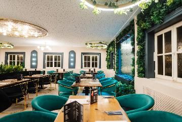 Ein stilvolles Restaurant mit modernen Möbeln und grünen Pflanzen. Die Tische sind ordentlich gedeckt und die Beleuchtung sorgt für eine angenehme Atmosphäre.