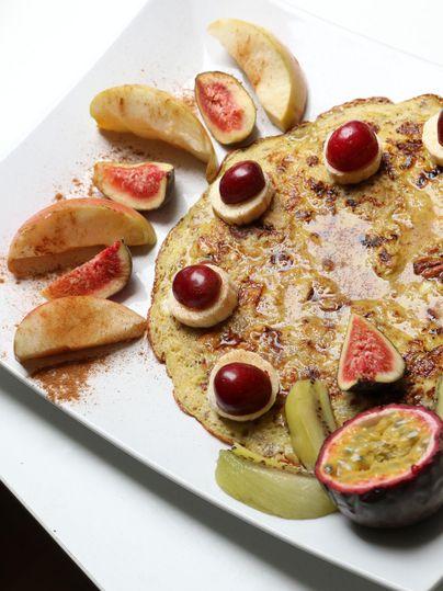 Pfannkuchen auf Teller mit Feigen, Apfelscheiben, Bananen und Kirschen dekoriert. Zimt ist über die Apfelscheiben gestreut.