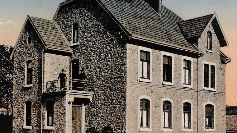 A historic stone parsonage with a balcony. The facade features several windows and a tiled roof.