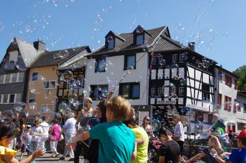 A lively marketplace full of people and soap bubbles. The colorful houses in the background give the scene a cheerful atmosphere.