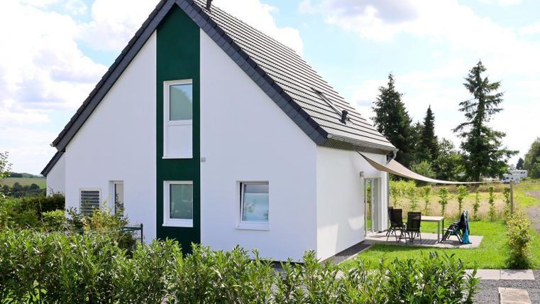 Ein modernes Haus mit einer weißen Fassade und grünem Akzent. Der Garten ist gepflegt und bietet eine Terrasse mit Gartenmöbeln.