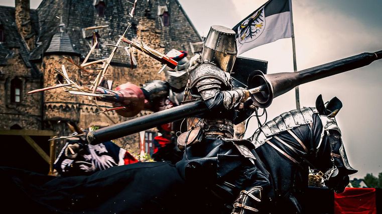 Een ridder in volle wapenrusting rijdt op een zwart paard en houdt een lans vast. Op de achtergrond is er een kasteel en een vlag te zien.