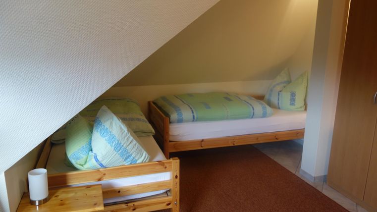 Een gezellige kamer met twee bedden en houten meubels. De muren zijn in zachte kleuren geschilderd.
