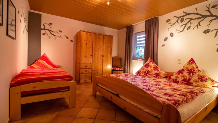 A cozy bedroom with a double bed and a single bed. The furniture is made of wood and the walls are decorated.