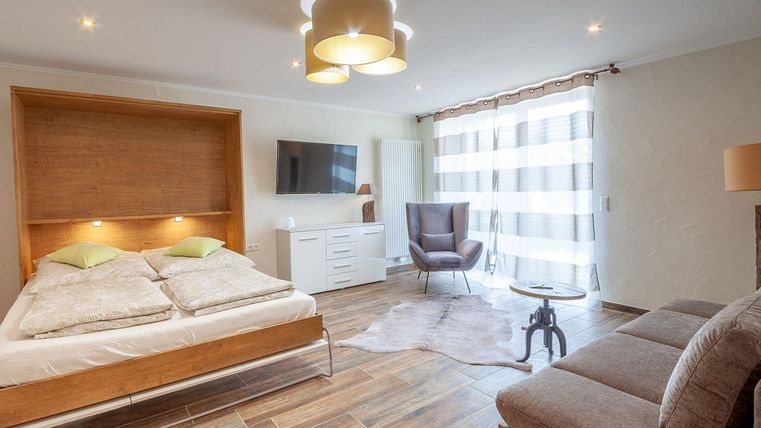 Ein modernes Zimmer mit einem Doppelbett und einer gemütlichen Sitzecke. Große Fenster lassen viel Licht herein, und das Holzdesign sorgt für eine warme Atmosphäre.