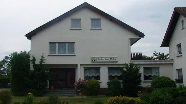 Een modern woonhuis met een lichte verf en twee verdiepingen. De tuin is goed onderhouden en aangelegd met verschillende planten.