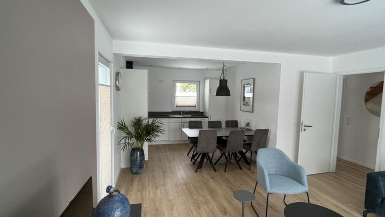 Ein modernes Wohnzimmer mit einem Essbereich. Es gibt einen großen Tisch mit Stühlen und eine helle, einladende Atmosphäre.