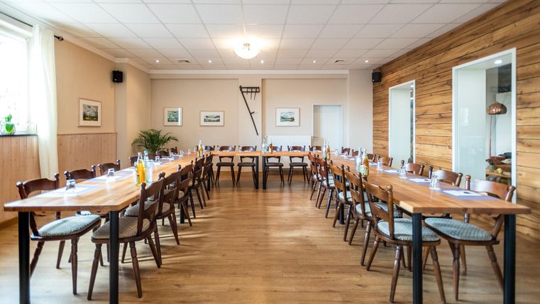 Een lichte vergaderzaal met lange tafels en veel stoelen. De wanden zijn deels van hout en er zijn planten ter decoratie.