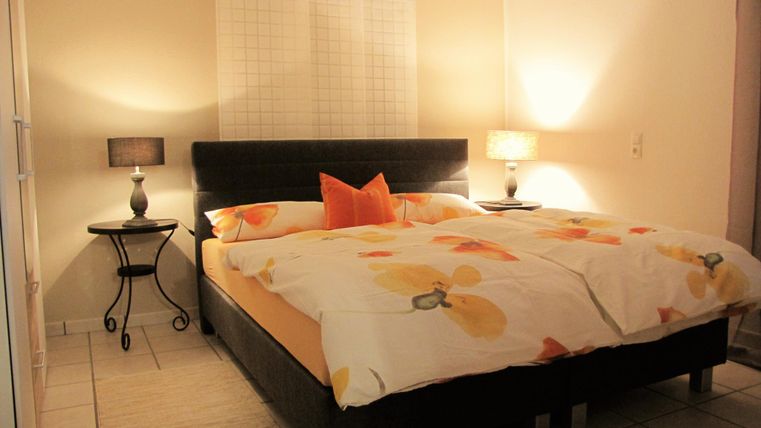 A cozy bedroom with a large bed and a colorful blanket. Next to the bed are nightstands with lamps.