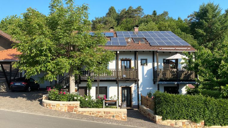 Een modern huis met zonnepanelen op het dak. Het staat in een rustige omgeving met groene bomen en een verzorgde tuin.