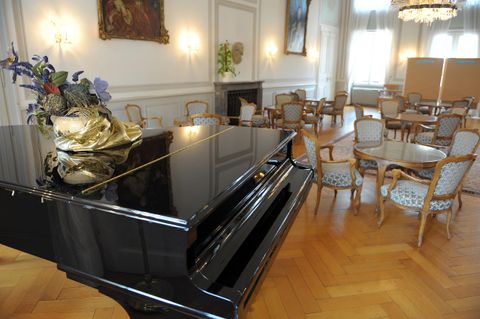 Een elegant piano staat in een stijlvolle kamer met een houten vloer. Rondom de piano bevinden zich gezellige tafels en stoelen.