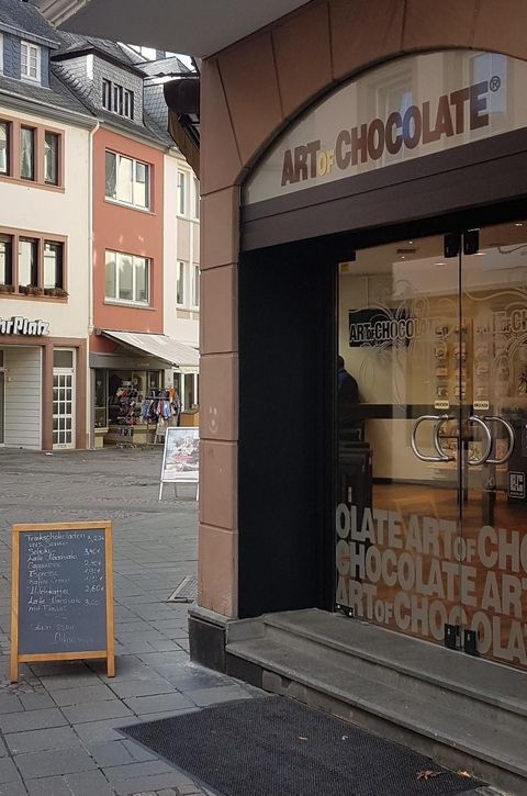 Ein Geschäft mit dem Namen „Art of Chocolate“ ist zu sehen. Draußen steht ein Holzbrett mit einer Speisekarte.