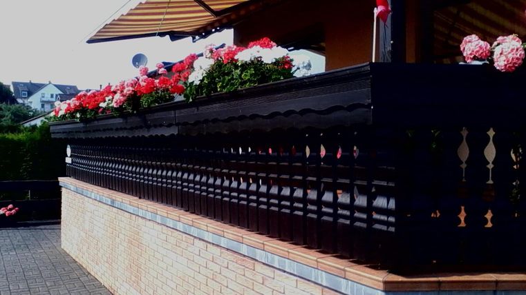 Een mooi balkon met kleurrijke bloembakken. Het terras heeft een elegante houten balustrade en is omgeven door een zonnige omgeving.
