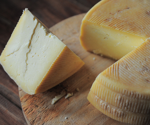 Ein großer Käseblock wurde angeschnitten und liegt auf einem Holztablett.