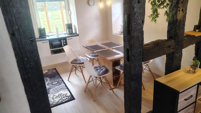 Eine helle Küche mit einem modernen Esstisch und Stühlen. Der Raum hat rustikale Holzbalken und große Fenster, die viel Tageslicht spenden.