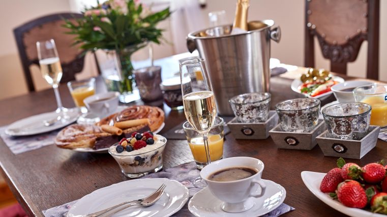 A beautifully set table with a fresh breakfast, including croissants, yogurt with berries, and fresh strawberries. Glasses with champagne and orange juice complete the picture.