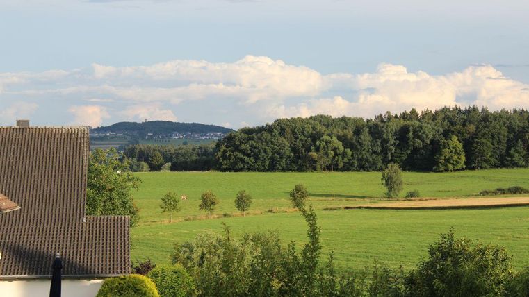 A peaceful landscape with green fields and trees. In the background, gentle hills and a cloudy sky can be seen.