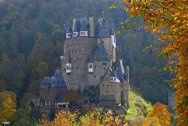 An imposing castle surrounded by colorful autumn trees. The landscape presents a picturesque backdrop with gentle hills.