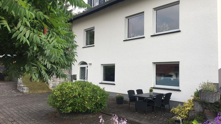 A modern house with white walls and large windows.
In front of the front door is a small garden with a seating area.