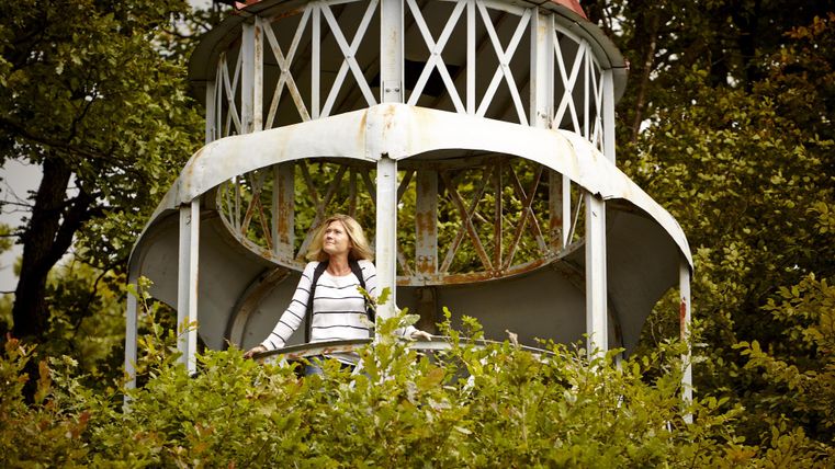 Eine Frau steht in einem Aussichtsturm, umgeben von grünen Pflanzen. Über ihr ist ein rotes Dach sichtbar.