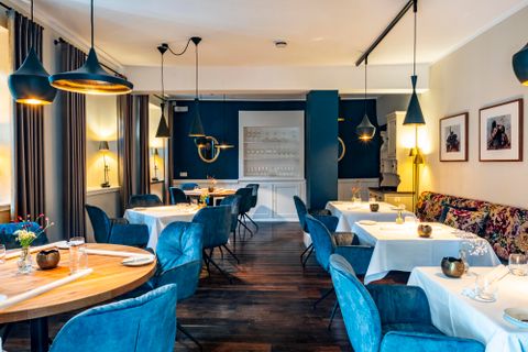 Een elegant restaurant met blauwe stoelen en mooi gedekte tafels. De warme lichten creëren een uitnodigende sfeer.