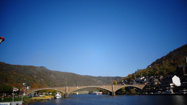 Eine malerische Brücke über einem ruhigen Fluss, umgeben von Hügeln. Der klare blaue Himmel verstärkt die Schönheit der Landschaft.