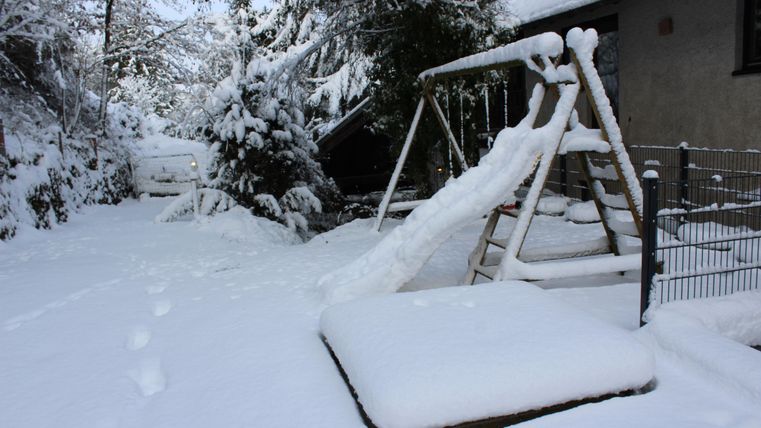 Ein Spielplatz im Schnee mit einer Rutsche und einer Schaukel. Der Garten ist von einer weißen Schneedecke bedeckt.