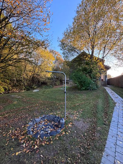 Ein Garten mit einem Holzhaus im Hintergrund und buntem Herbstlaub. In der Mitte steht ein Wasserhahn auf einem kleinen Steinring.