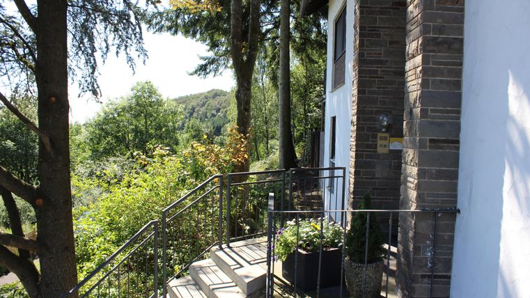 Ein Treppenaufgang mit einem Geländer führt zu einem modernen Gebäude. Umgeben von Bäumen und grüner Landschaft bietet der Ort einen ruhigen Ausblick.