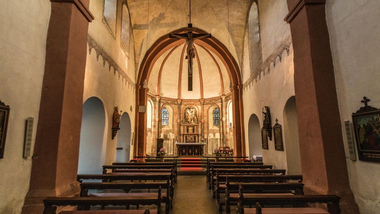 Innenansicht der Kirche im Kloster Niederehe, mit Altar, Bänken und Kreuz. Die Wände sind schlicht, mit Buntglasfenstern im Hintergrund.