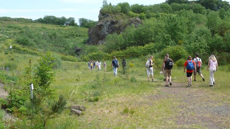 Menschen wandern durch eine grüne Landschaft mit Hügeln und Bäumen im Vulkangarten.
