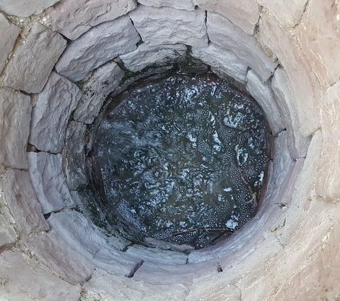 Ein tiefer Brunnen mit steinernen Wänden und klarem Wasser. Kleine Wasserbewegungen sind an der Oberfläche sichtbar.