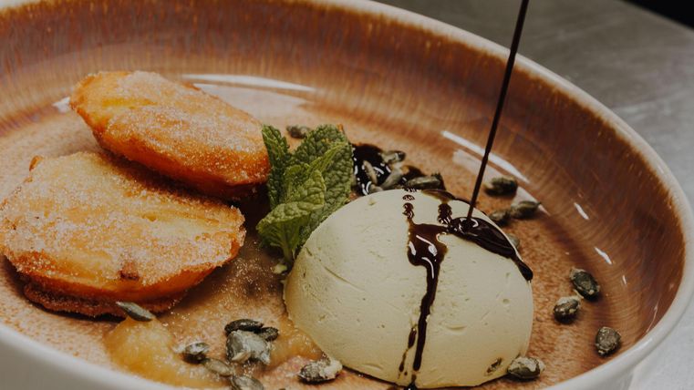 Ein Dessertteller mit goldbraunen Apfel Beignets und Kürbiskernparfait. Mit Kürbisöl und frischer Minze dekoriert.