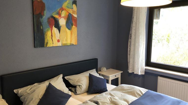 Een gezellige slaapkamer met een groot bed en kleurrijke kunst aan de muur. De ruimte is helder en vriendelijk, met een raam en een lamp die voor aangenaam licht zorgen.