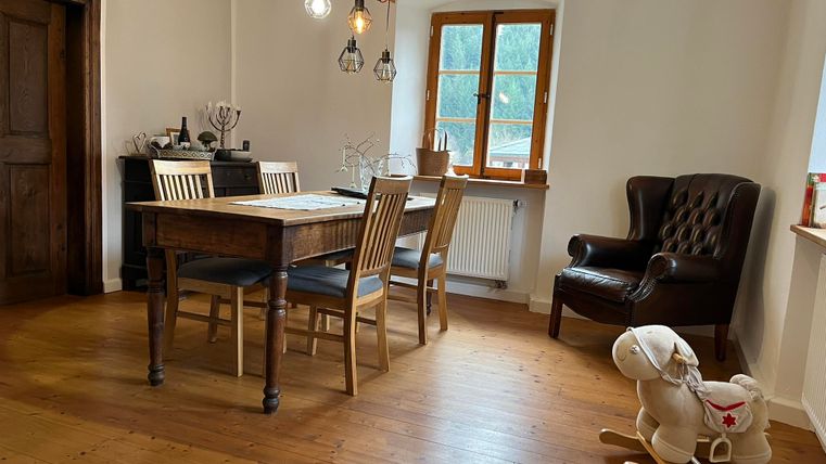 Ein gemütlicher Raum mit einem Holztisch und Stühlen. Im Hintergrund steht ein Schaukelpferd und ein gemütlicher Sessel.