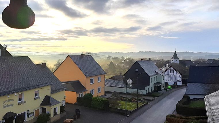 A picturesque village with colorful houses and gentle hills in the background. The sky is cloudy and radiates a soft light.