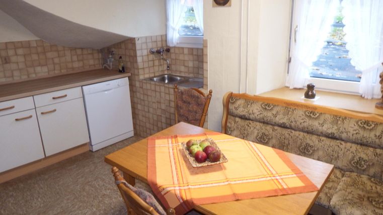 A bright kitchen nook with a table and a cozy bench. The kitchen is well-equipped with a stove, a dishwasher, and windows for daylight.